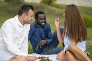 Menschen sitzen auf einer Picknickdecke draußen zusammen, essen und unterhalten sich.